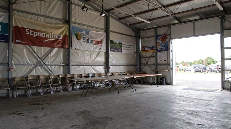 An empty regional showground pavilion with banner frames, stacked chairs and a long table before an open day